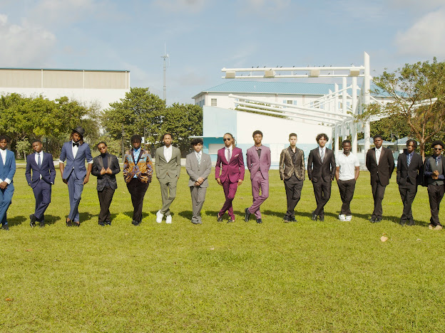 Young Men of Distinction participants in colorful suits lined up on a grass field
